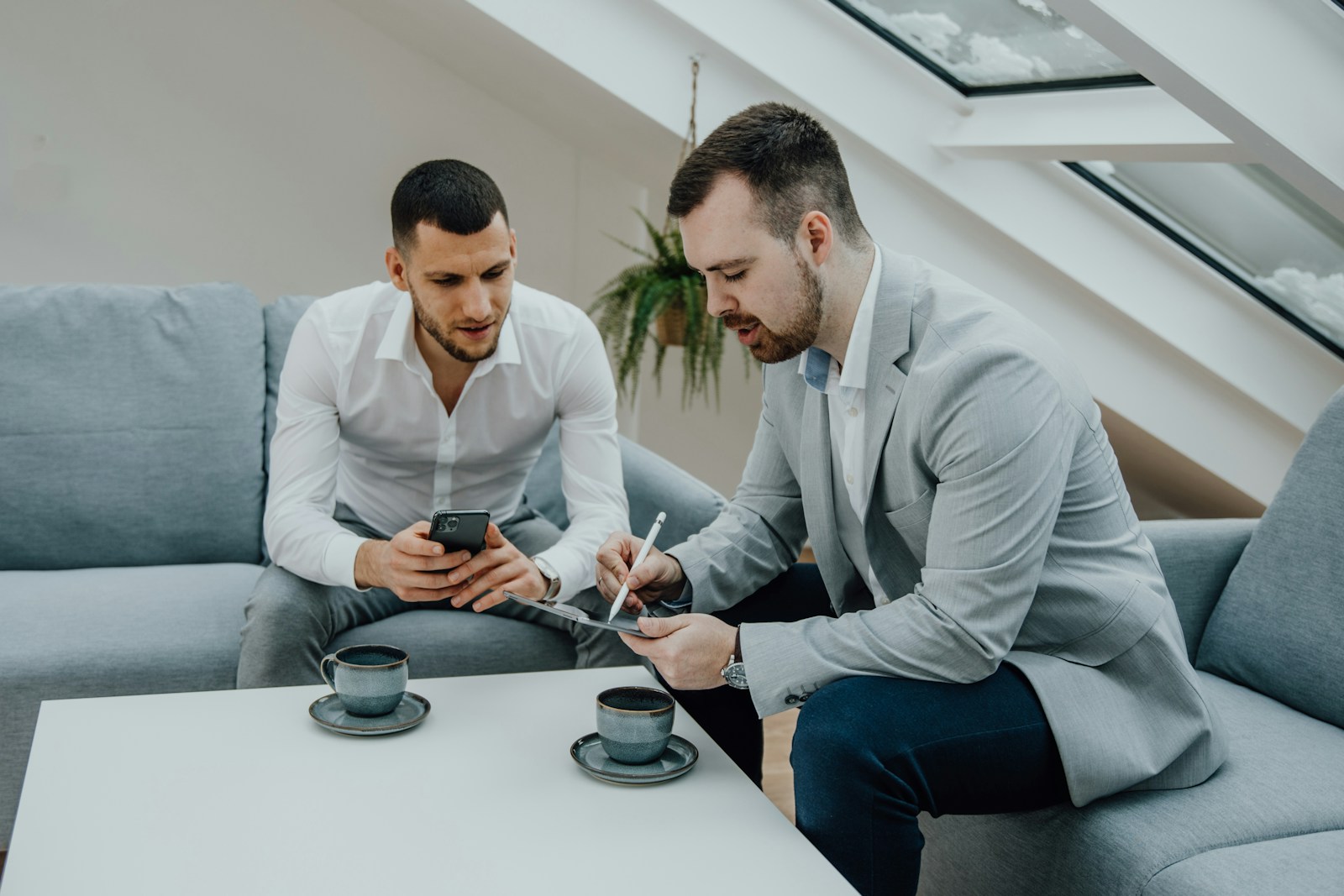 two men sitting on a couch looking at a cell phone